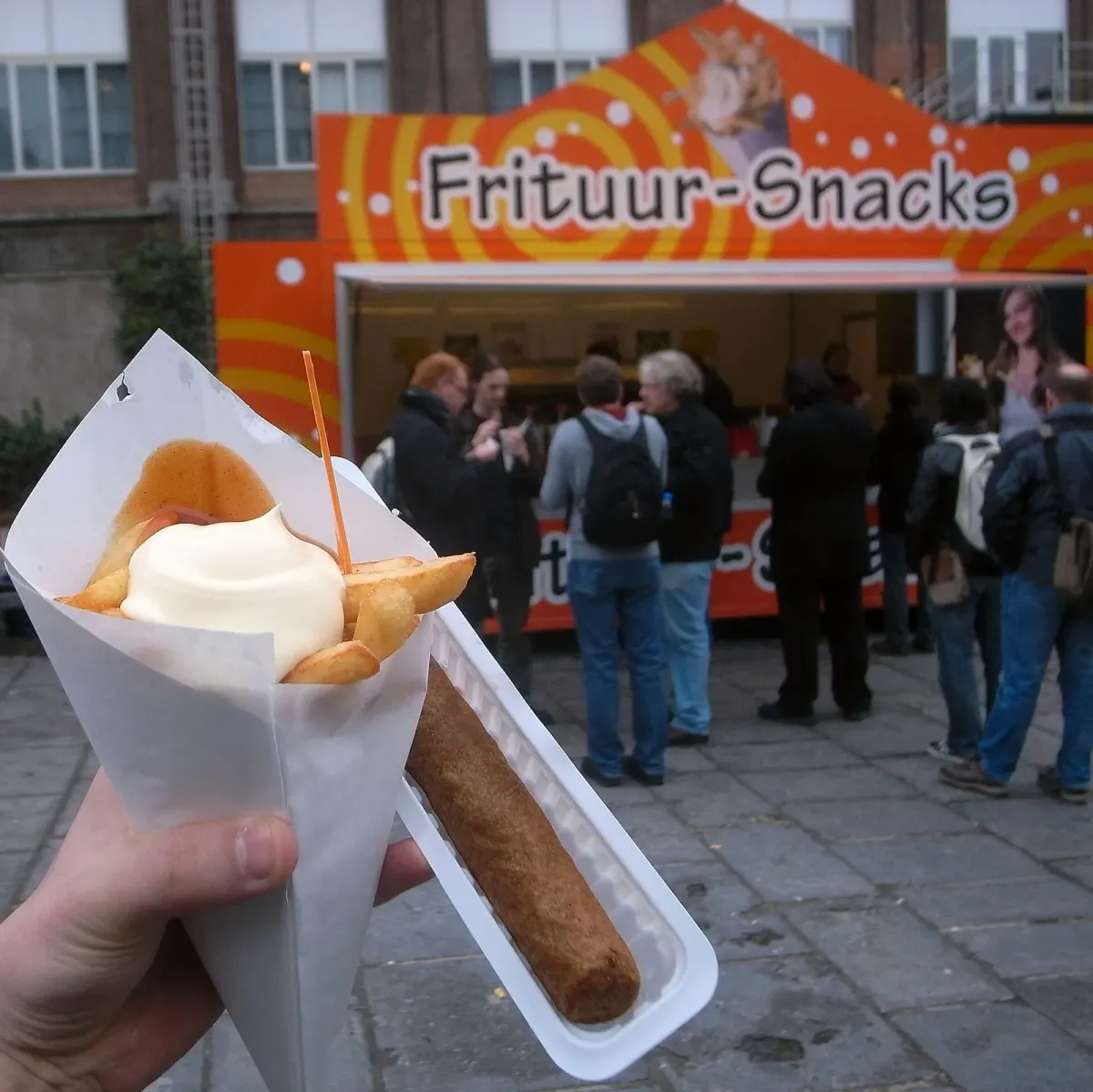 Cornet de frites belges garni de sauce, posé sur le comptoir d'une friterie